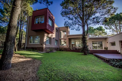 Fachada moderna con volumen rojo y grandes ventanales — proyecto Vivienda Unifamiliar en Pinamar, por Estudio Schifano, en Pinamar