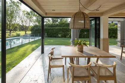Comedor exterior con pérgola de madera, vista a la piscina y gran lámpara colgante — proyecto Quincho PG, por Estudio Lak
