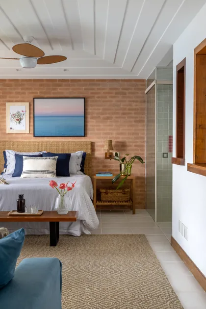 Dormitorio moderno con pared de ladrillo visto y baño integrado — proyecto Casa da Ilha, por Miguel Capanema Arquitetura