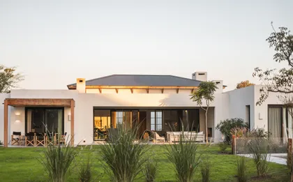 Fachada moderna de casa con amplios ventanales y jardín exuberante — proyecto Casa LC, por SBMT, en Pilar