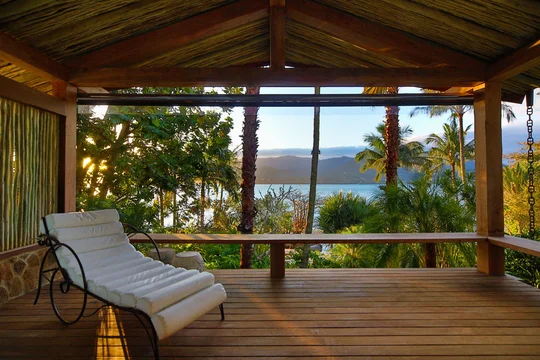 Terraza de madera con vista al lago entre palmeras y montañas — proyecto Arquitetura e Interiores I, por Demian Golovaty