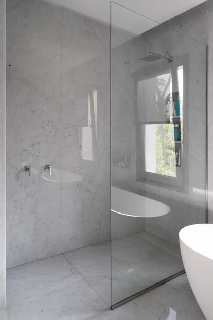Baño moderno con paredes de mármol, bañera exenta y ventana grande — proyecto Casa AE, por Ricardo Pereyra Iraola 