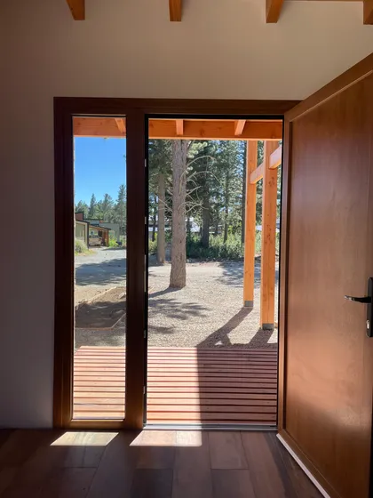 Puerta de madera con vista a bosque y deck de madera — proyecto Mountain House, por Arquitecta Grace Overgaard, en San Carlos de Bariloche