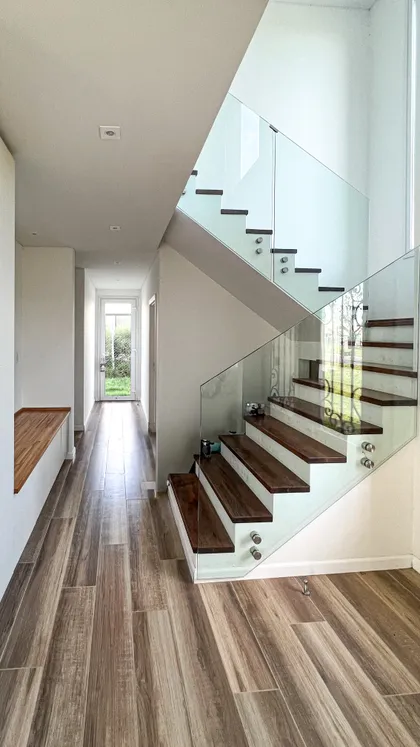Escalera moderna con pasamanos de vidrio, piso de madera oscura y luz natural — proyecto Casa Hipico, por RY Construir Estudio, en Pilar