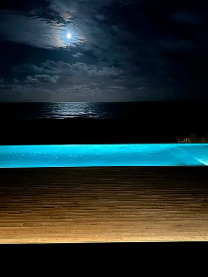Piscina infinita iluminada bajo la luna junto a terraza de madera — proyecto CASA sobre el MAR, por Guerrero Arquitectos, en Pinamar