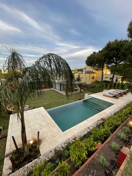 Piscina infinita moderna con deck de piedra y vegetación exuberante — proyecto COSTA ESMERALDA, por Baires Green, en Pinamar