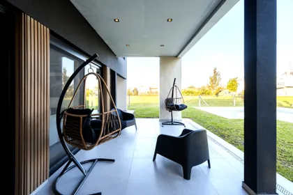 Terraza moderna con sillas colgantes de ratán y detalles en madera — proyecto Casa ALM57, por EZ architects, en Canning