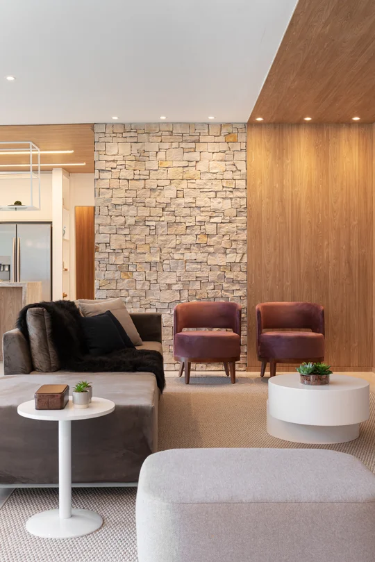 Living moderno con pared de piedra, muebles en tonos cálidos y madera — proyecto Decorados Vitória, por Pricila Dalzochio