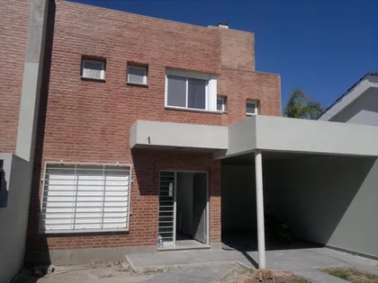 Fachada de casa moderna con ladrillo expuesto y cochera — proyecto Duplex granja de Funes, por Gustavo Gurvich Arquitecto, en Córdoba