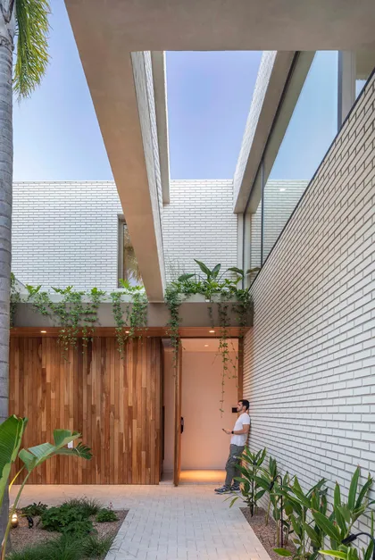 fachada moderna con puerta pivotante de madera y ladrillo blanco — proyecto Casa Magnolia, por Estudio PK, en San Isidro