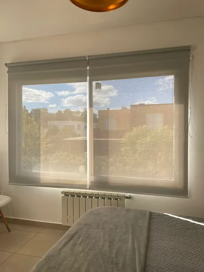 Dormitorio moderno con persianas translúcidas y cama grande — proyecto ROLLER SUNSCREEN 5% PREMIUM COLOR GRIS/GRIS, por Cortinas Oeste Roller, en Pilar