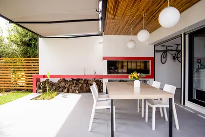 Comedor exterior moderno con parrilla integrada y techo de madera — proyecto CASA GONNET, por LEONE LORAY ARQUITECTOS, en Gonnet