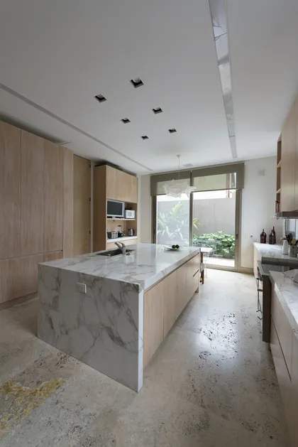 Cocina moderna con isla de mármol y gabinetes de madera integrados — proyecto Casa H, por Estudio Dado, en Belgrano