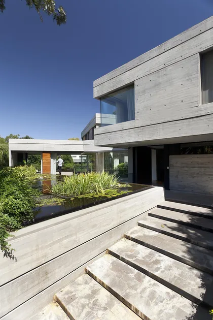 Casa moderna de hormigón visto con estanque y amplias ventanas — proyecto Acasusso, por Remy Arquitectos, en Acassuso