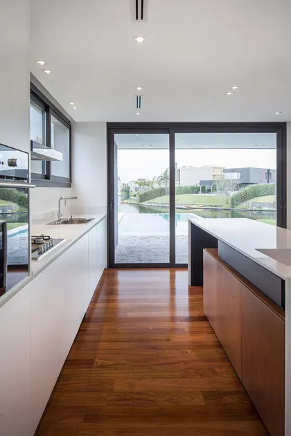 Cocina moderna con isla y vista al agua, pisos de madera — proyecto Alisos, por Remy Arquitectos, en Nordelta