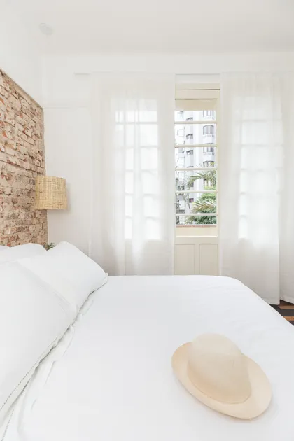 Dormitorio minimalista con cabecera de ladrillo visto y balcón — proyecto Roomie Coliving, por Camila Cavalheiro Arquiteta