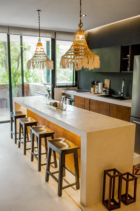 Cocina moderna con isla blanca, lámparas tejidas y banquetas de madera — proyecto Tropical Moroccan Paradise, por Interiors Tulum