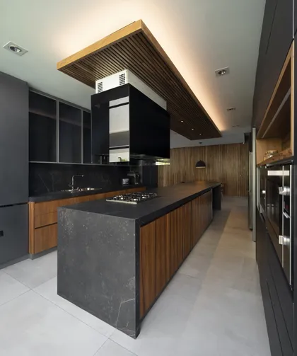 Cocina moderna con isla de piedra, madera y campana negra — proyecto Casa L Golf, Nordelta, por Estudio Gambotto, en Nordelta