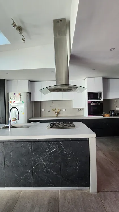 Cocina moderna con isla de mármol oscuro y campana extractora central — proyecto Casa Berner, por Zima Arquitectura, en La Plata