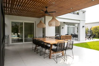 Comedor exterior con mesa de madera y sillas de mimbre, bajo techo de madera — proyecto Obra Newman J, por Arq. Lourdes Yarade Saravia, en Benavidez
