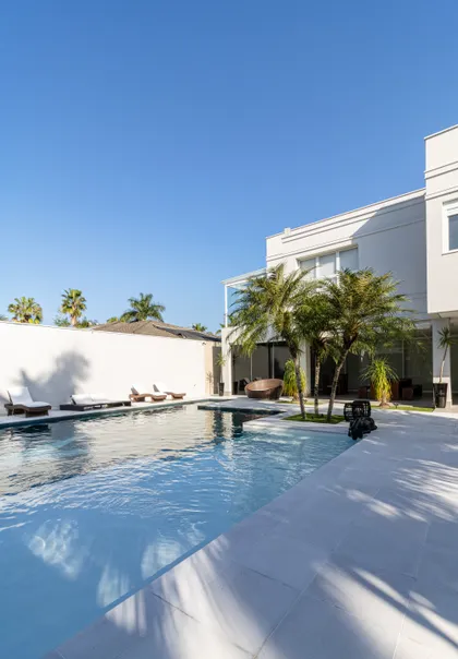 Amplia vista de piscina moderna con tumbonas blancas y vegetación — proyecto Mansão de Gabigol, por Carlos Pardal, en Guarujá