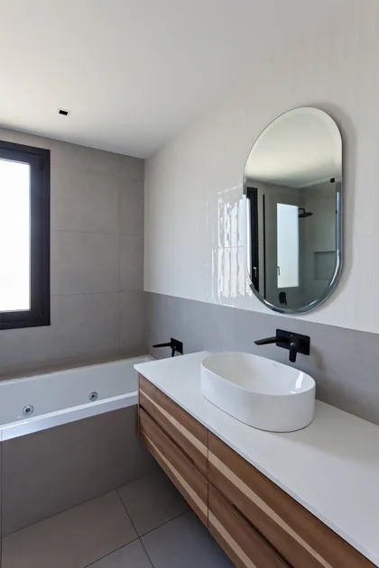 Baño moderno con espejo ovalado y vanitory de madera — proyecto CASA RDV, por Rastro Estudio, en San Isidro