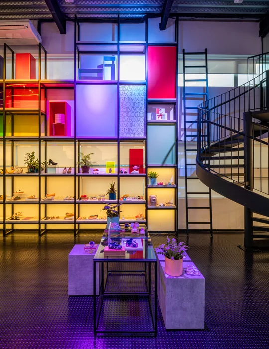 Local comercial iluminado con estanterías modernas de colores y escalera helicoidal — proyecto Showroom Melissa, por Pricila Dalzochio