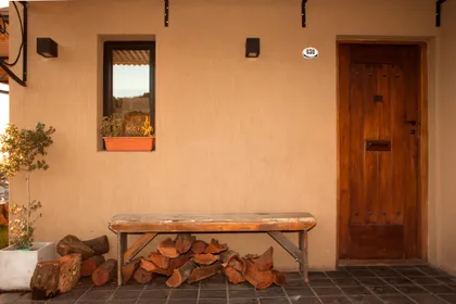 fachada de casa mediterranea con leña y banco de madera — proyecto Inmuebles, por Geo Estudio, en Buenos Aires
