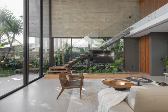 Living contemporáneo con ventanal doble altura, vegetación interior y mobiliario madera — proyecto Casa M.J., por Ruschel Arquitetura e Urbanism
