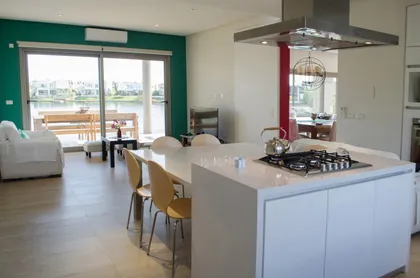 Cocina moderna abierta con vista al agua y isla blanca — proyecto Casa Nordelta, por linearecta.arquitectura, en Nordelta