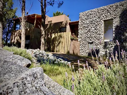 Casa de campo con fachada de piedra, madera y ladrillo, rodeada de lavanda — proyecto Los Medanos Necochea, por Marconi Silva Arquitectos, en Necochea