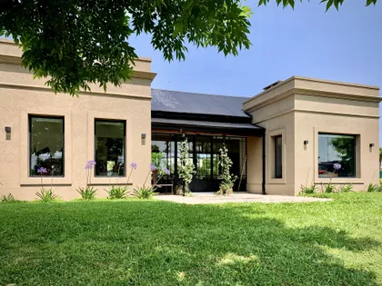 Fachada moderna color beige con grandes ventanales y jardín frontal — proyecto Los Jazmines Pilar del Este, por Marconi Silva Arquitectos, en Pilar del Este