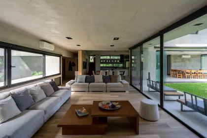 Living moderno con techos de hormigón y amplios ventanales — proyecto Casa Miralagos II, por Besonías Almeida arquitectos, en La Plata