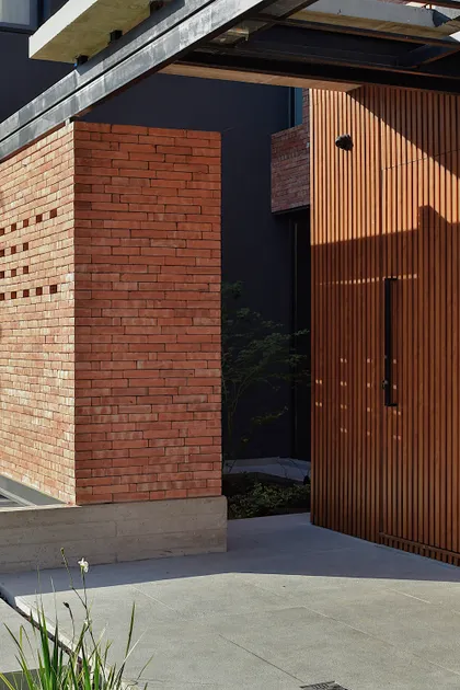 Fachada moderna con ladrillo visto y puerta de madera listonada — proyecto CASA HC, por Daniel Daniele - Oficina de Arquitectura, en Canning