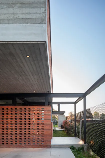 Fachada moderna con ladrillo perforado, concreto expuesto y pérgola de metal — proyecto CASA BSB, por BUSCETTI & DI BERNARDO arquitectas, en Gonnet