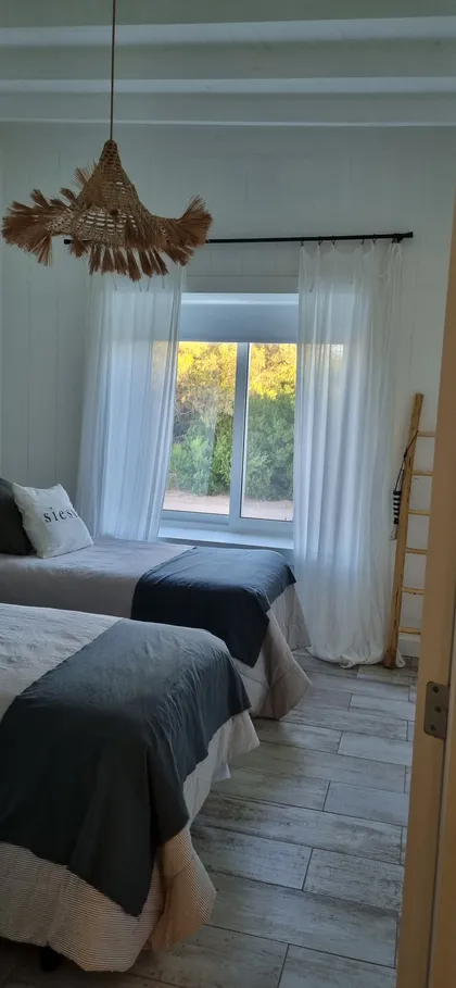 Dormitorio con dos camas, luz tejida y ventana al exterior — proyecto Casa costa, por Trazarq, en Pinamar