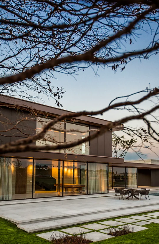 Casa moderna con fachada vidriada y terraza de hormigón al atardecer — proyecto Arquitetura e Interiores II, por Demian Golovaty