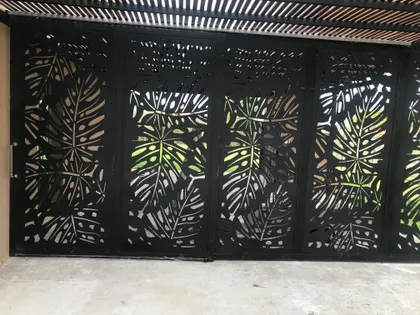 fachada moderna con portón de metal calado y vegetación — proyecto Chapa calada decorativa, tríptico árbol de la vida oara portones corredizos y ce, por Pintastic, en Belén de Esco