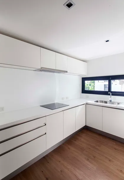 Cocina minimalista moderna con muebles blancos y anafe de inducción — proyecto Alvear AV, por V2 Arquitectos, en City Bell