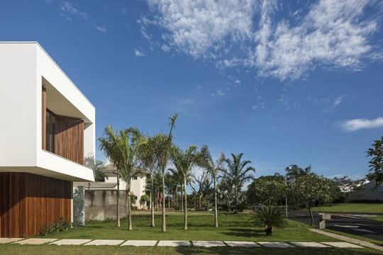 Casa contemporánea blanca con jardín, palmeras y cielo despejado — proyecto Casa Olhos D'água, por Aguirre Arquitetura