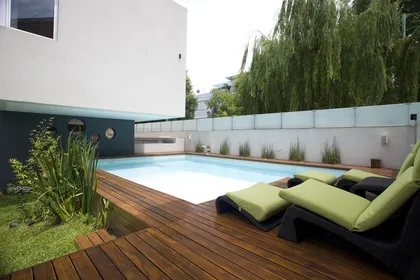 piscina moderna con deck de madera y vegetación exuberante — proyecto Devoto, por Remy Arquitectos, en CABA
