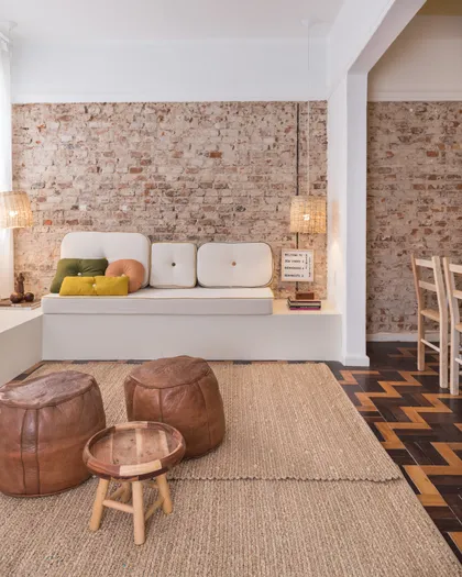 Living con muros ladrillo visto, asientos blancos y puffs cuero marrón — proyecto Roomie Coliving, por Camila Cavalheiro Arquiteta
