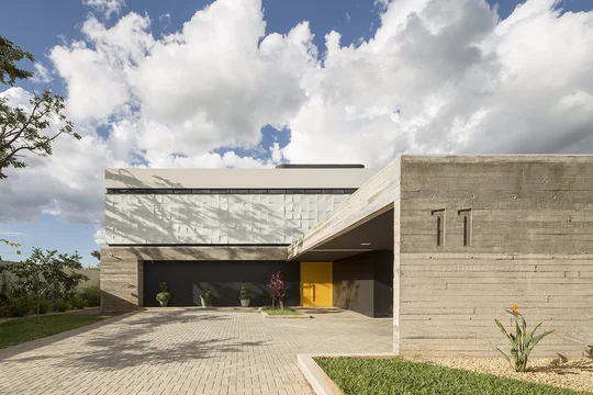 Casa moderna en hormigón visto con acceso amarillo y patio enlosado — proyecto Casa 11, por Coda Arquitetos