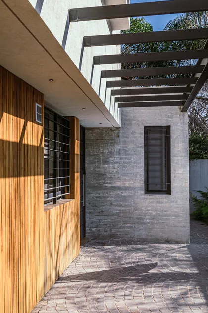 Fachada moderna con madera y hormigón visto, pérgola y patio empedrado — proyecto Casa La Horqueta, por LSA. , en San Isidro