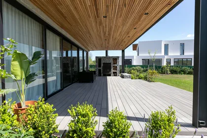 Amplio deck de madera gris con techo de listones de madera natural y chimenea exterior — proyecto La volanta 152, por ATO Arquitectos