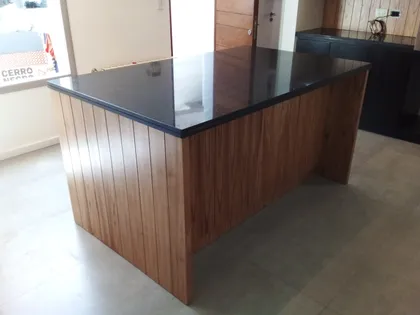 Isla de cocina moderna con revestimiento de madera y mesada negra — proyecto cocina en paraiso con detalles negros, por Dnni, en Gonnet