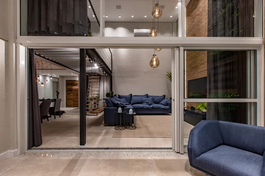 Living moderno con sofá azul, ventanal doble altura y ladrillo visto — proyecto Duo Morumbi, por Pricila Dalzochio