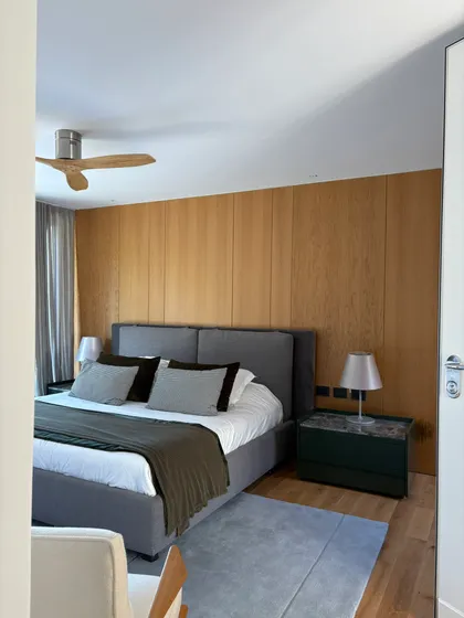 Dormitorio moderno con paredes de madera, cama gris y sillón blanco — proyecto Peru, por ABEJA CONCEPT, en B1641 Acassuso
