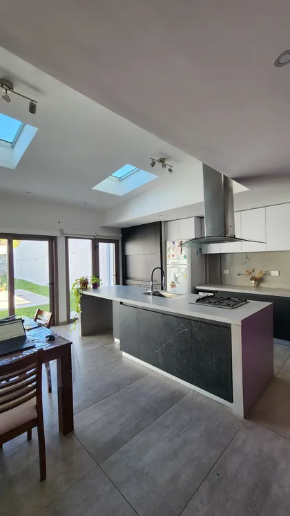 Cocina moderna abierta con isla, claraboyas y puerta a jardín — proyecto Casa Berner, por Zima Arquitectura, en La Plata