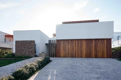 Fachada moderna con puerta de garaje de madera y hormigón blanco — proyecto Construcciones, por Artime Arquitectura, en Pilar